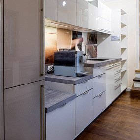 Moderne Einbauküche mit weißen Hochglanzfronten, Holzboden und Kaffeemaschine.