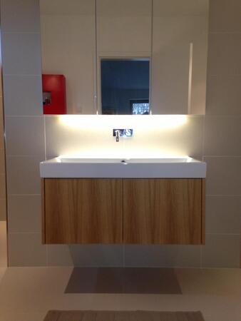 Modernes Badezimmer mit beleuchtetem Spiegel, Waschtisch aus Holz und Wandarmatur.