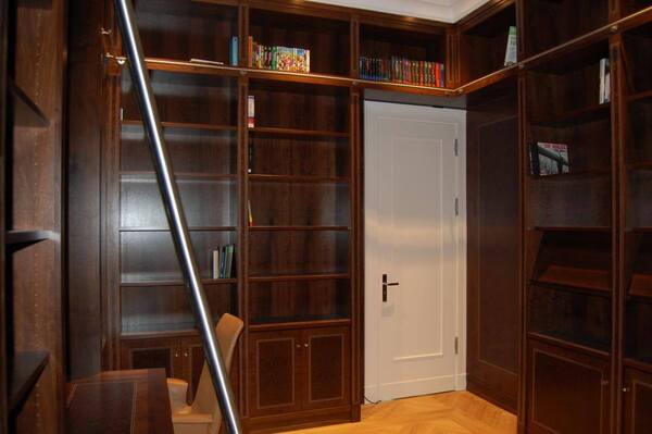 Bibliothek mit dunklen Holzregalen, wenigen Büchern und Leiter vor weißer Tür.