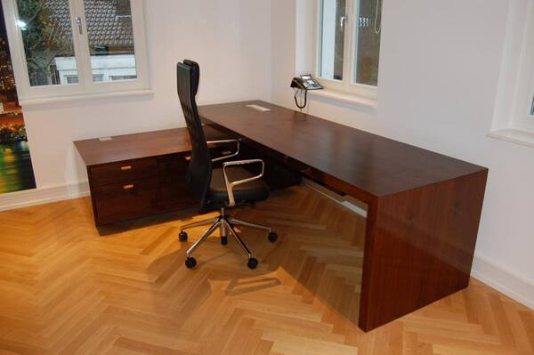 Modernes Büro mit großem Eckschreibtisch aus Holz, ergonomischem Stuhl und Parkettboden.