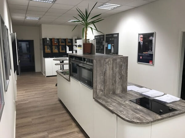 Moderne Küchenausstellung mit Kochfeld, Einbaugeräten und Musterflächen auf Holzoptik.