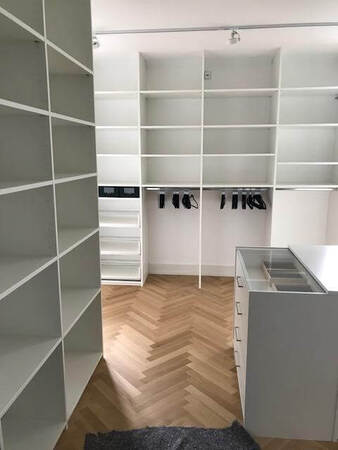 Moderner begehbarer Kleiderschrank mit weißen Regalen und Schubladen auf Parkettboden.