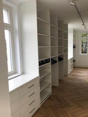 Moderner, begehbarer Kleiderschrank mit weißen Regalen und Schubladen auf Parkettboden.