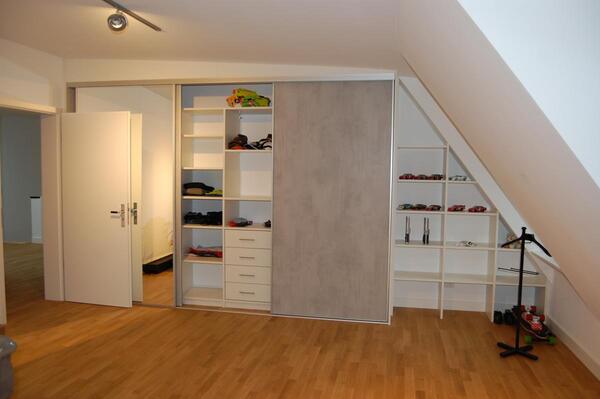 Ein moderner Einbauschrank mit offenen Regalen und Schiebetüren unter einer Dachschräge.